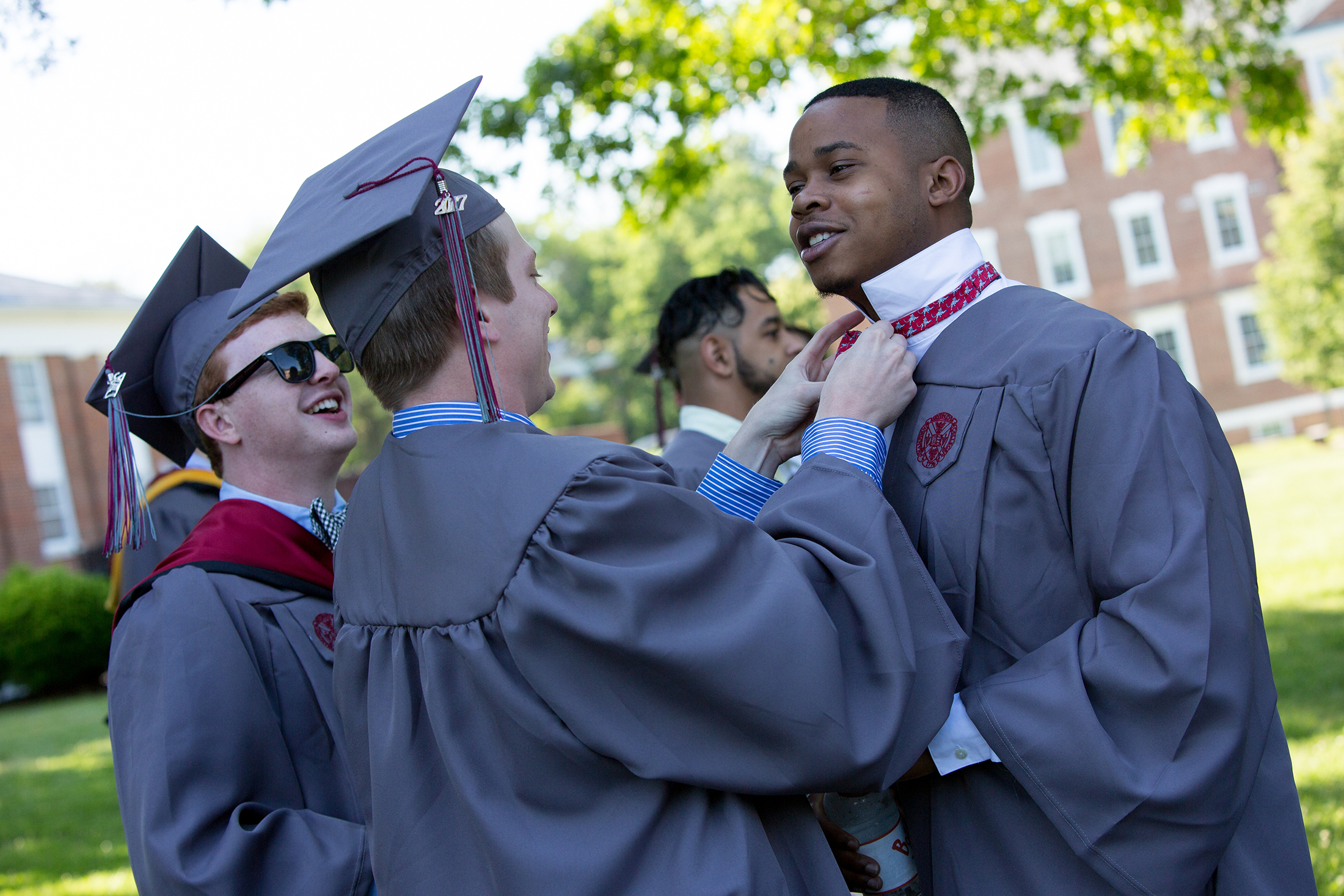 Three men in graduation gowns, with one tying another's bow tie
