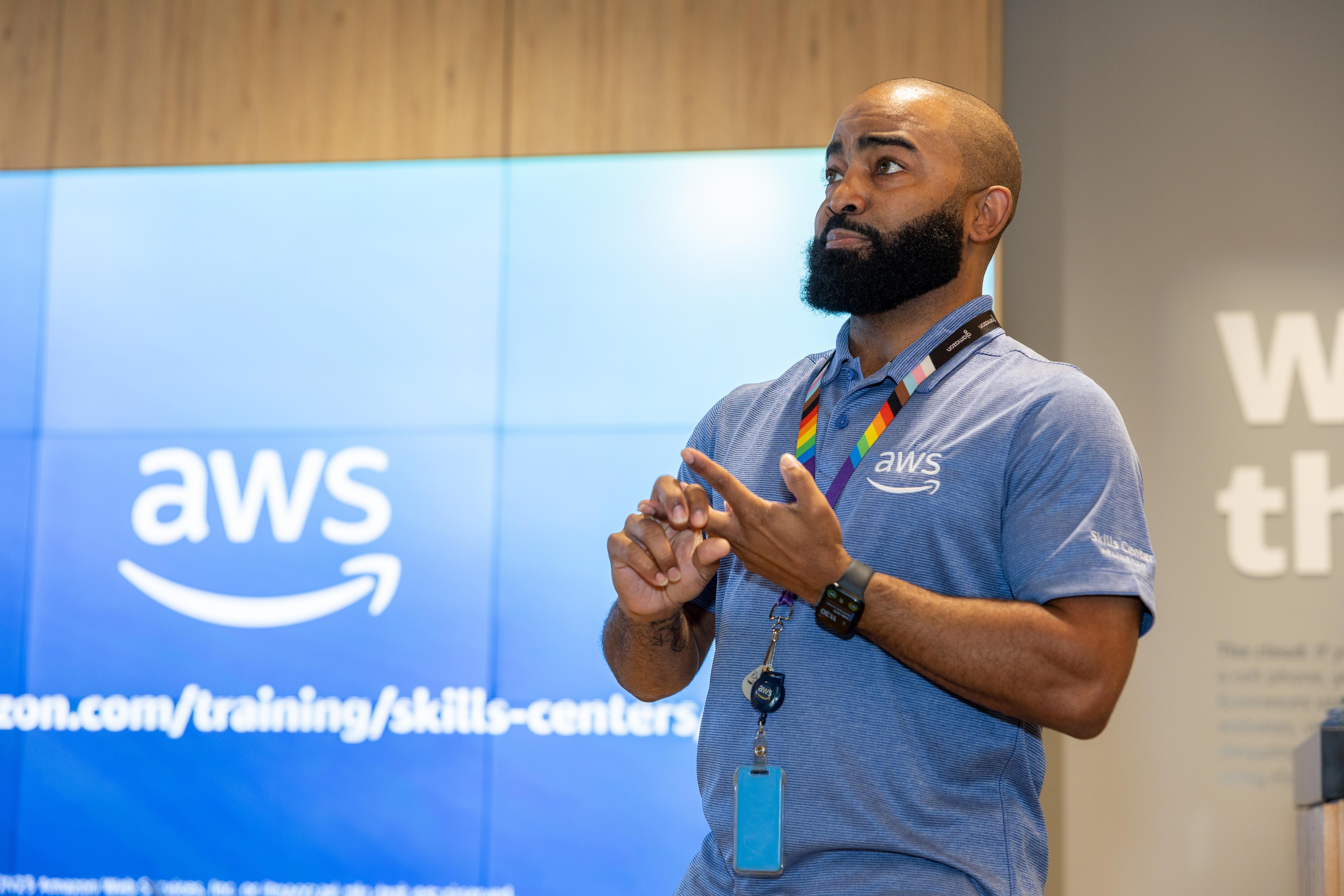 A man standing in front of a computer wall with the Amazon Web Services logo