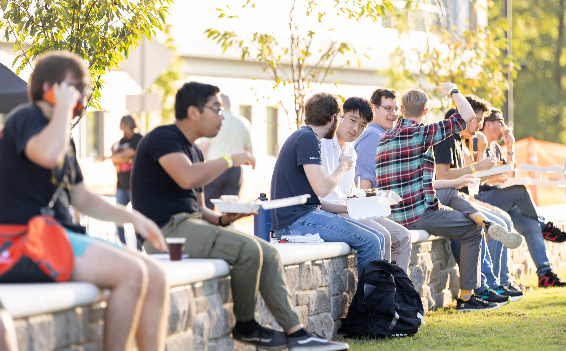 People talking to each other while sitting on a short stone wall