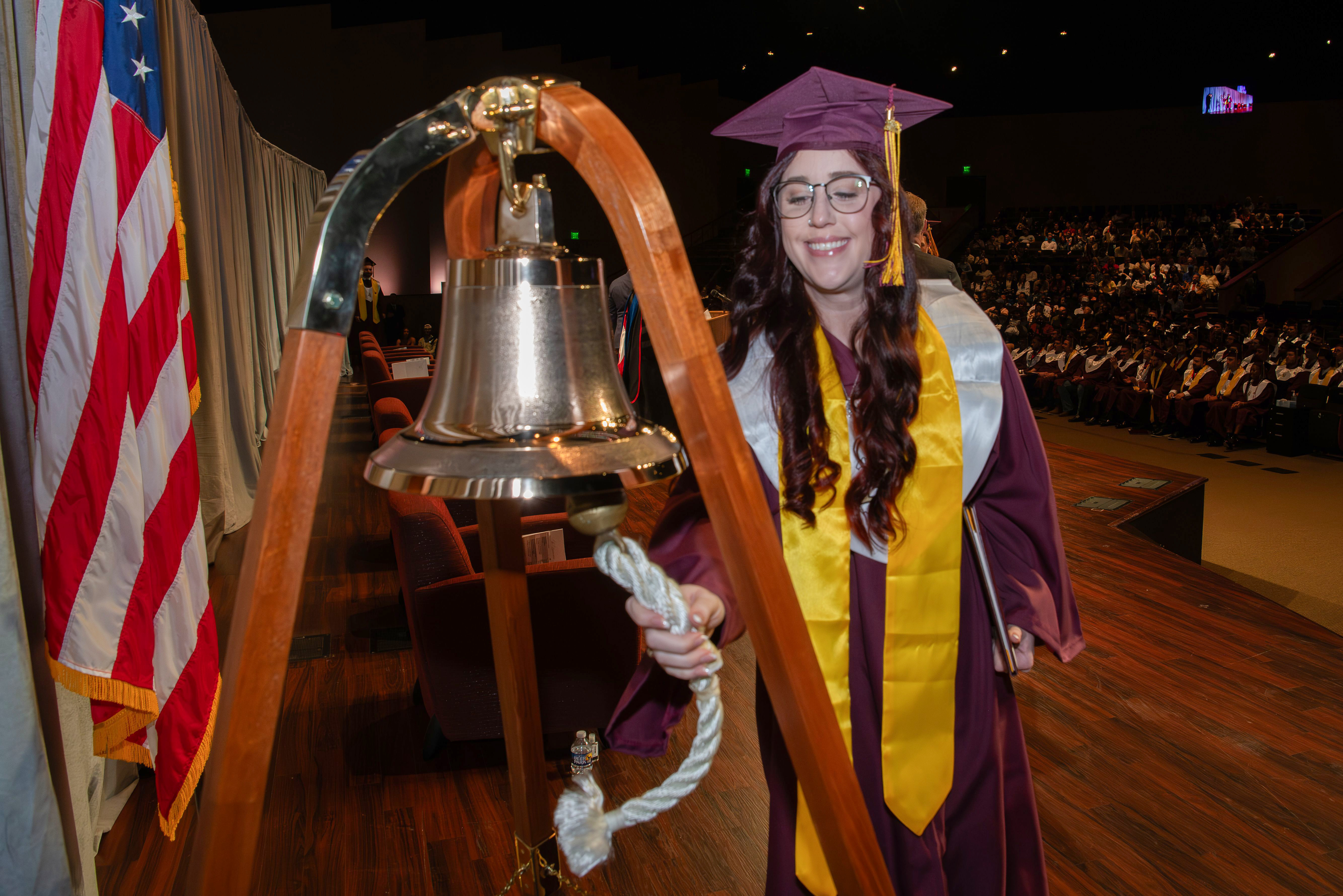 Photo of a female college graduate ringing a bell