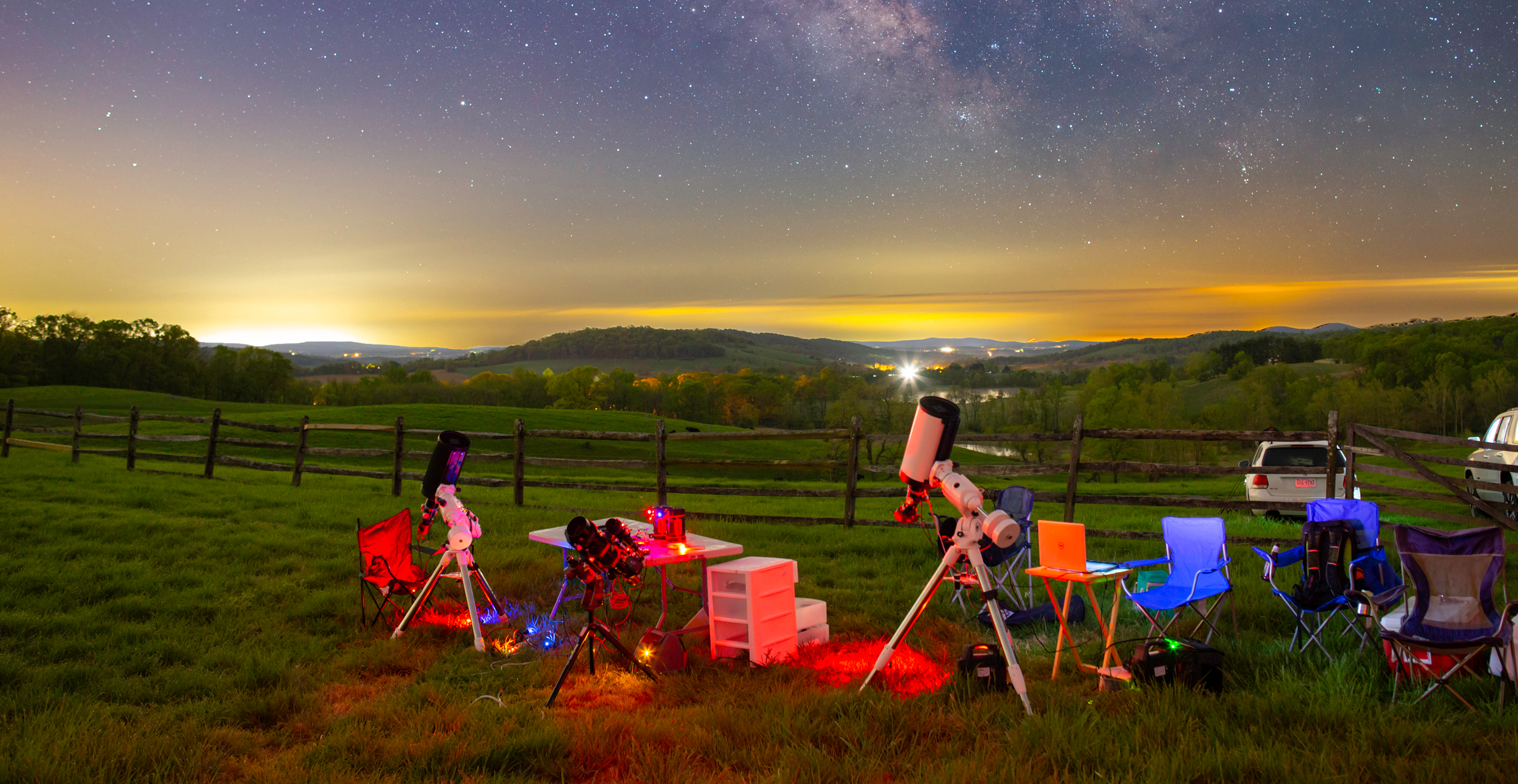 Telescopes set up in a field beneath a star-filled night sky.