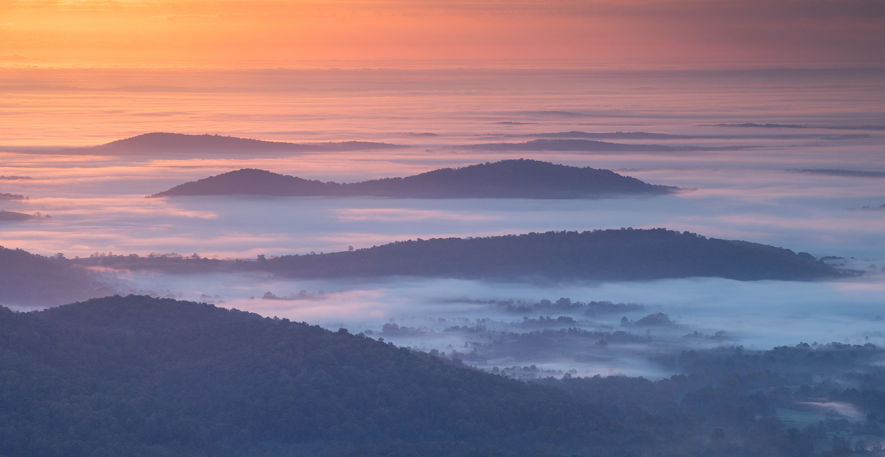 Fog drifting through layered mountain ridges at sunrise.