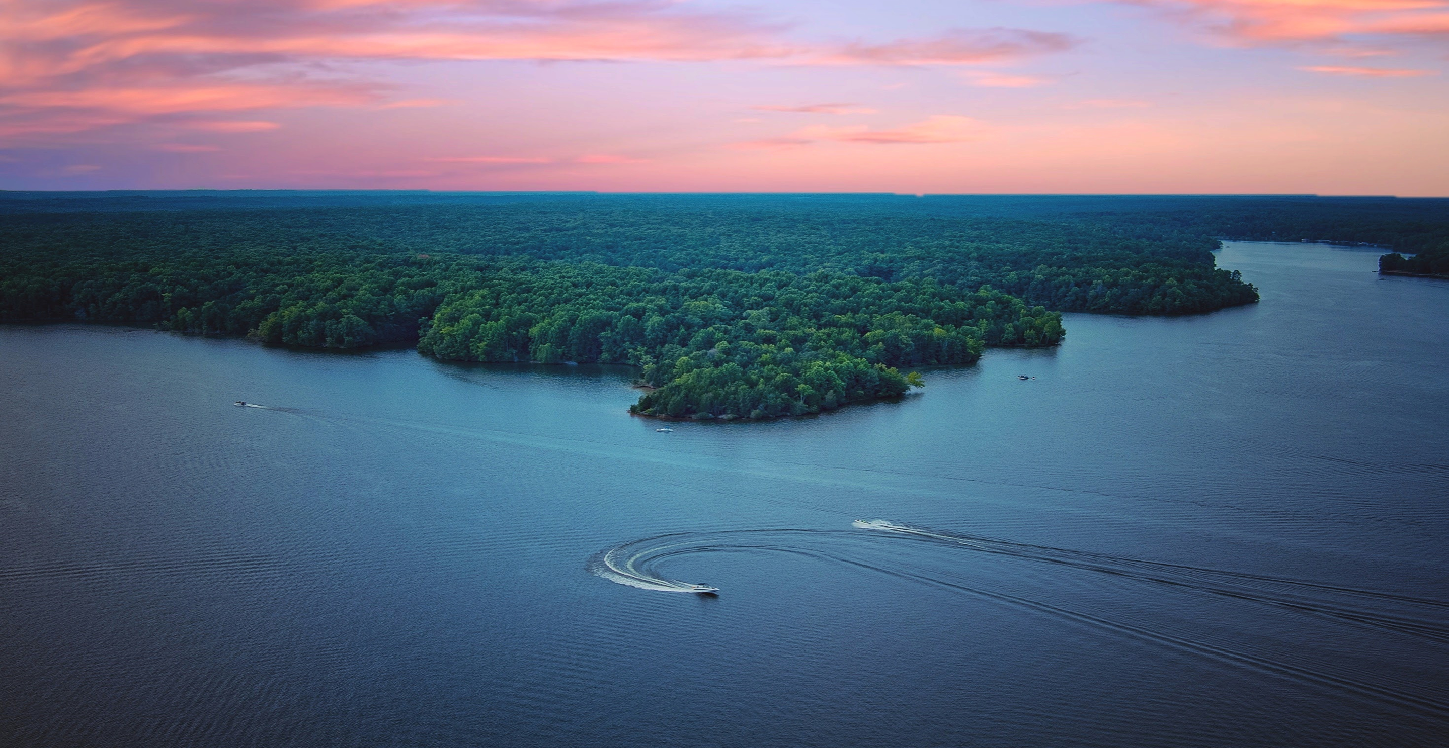 Boats traveling across a large lake surrounded by forest.
