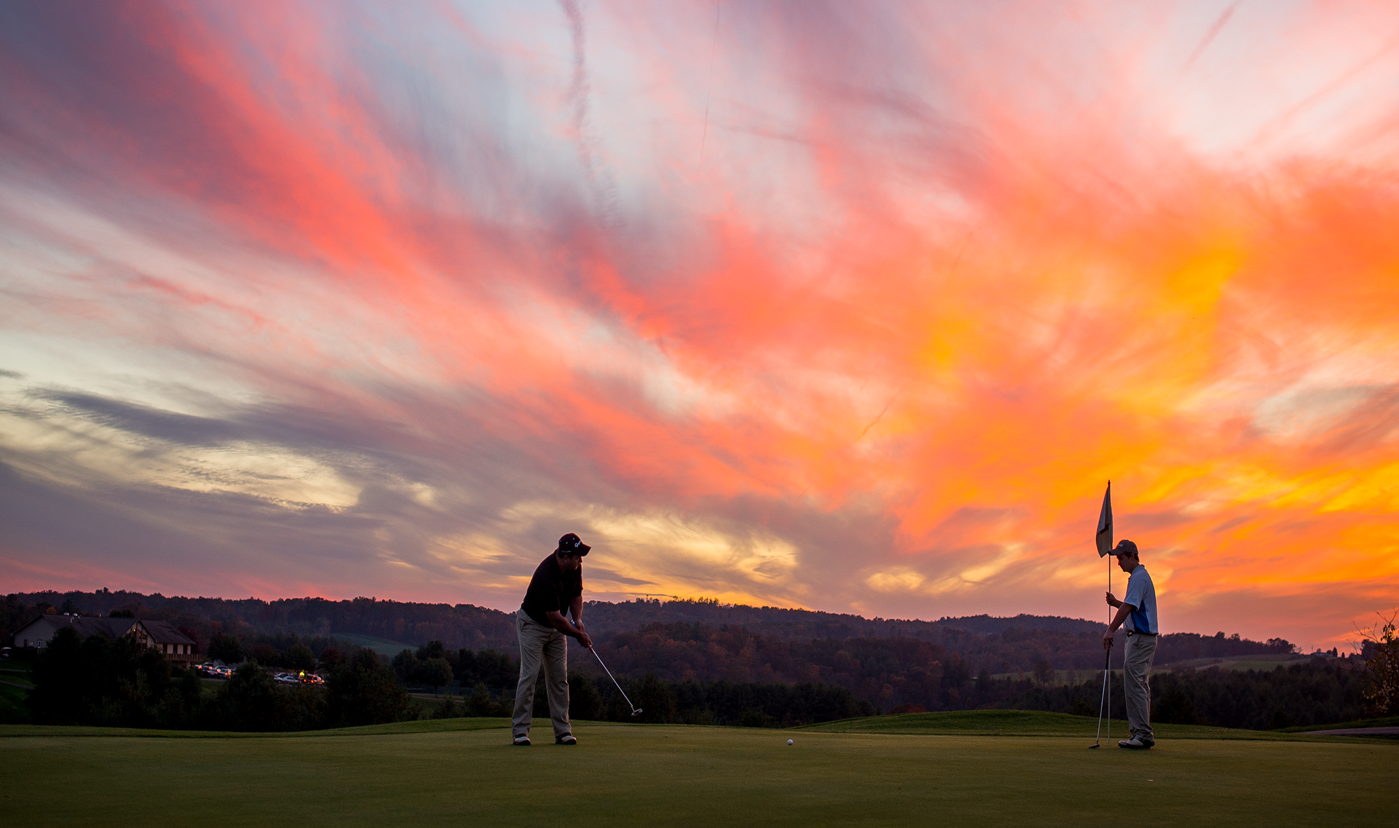 Golfing putting on a green beneath a pink sky