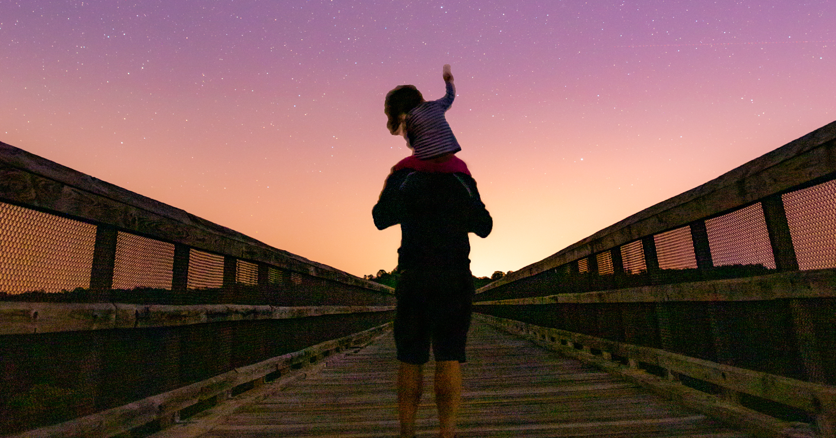 Child on father's shoulders pointing to the stars