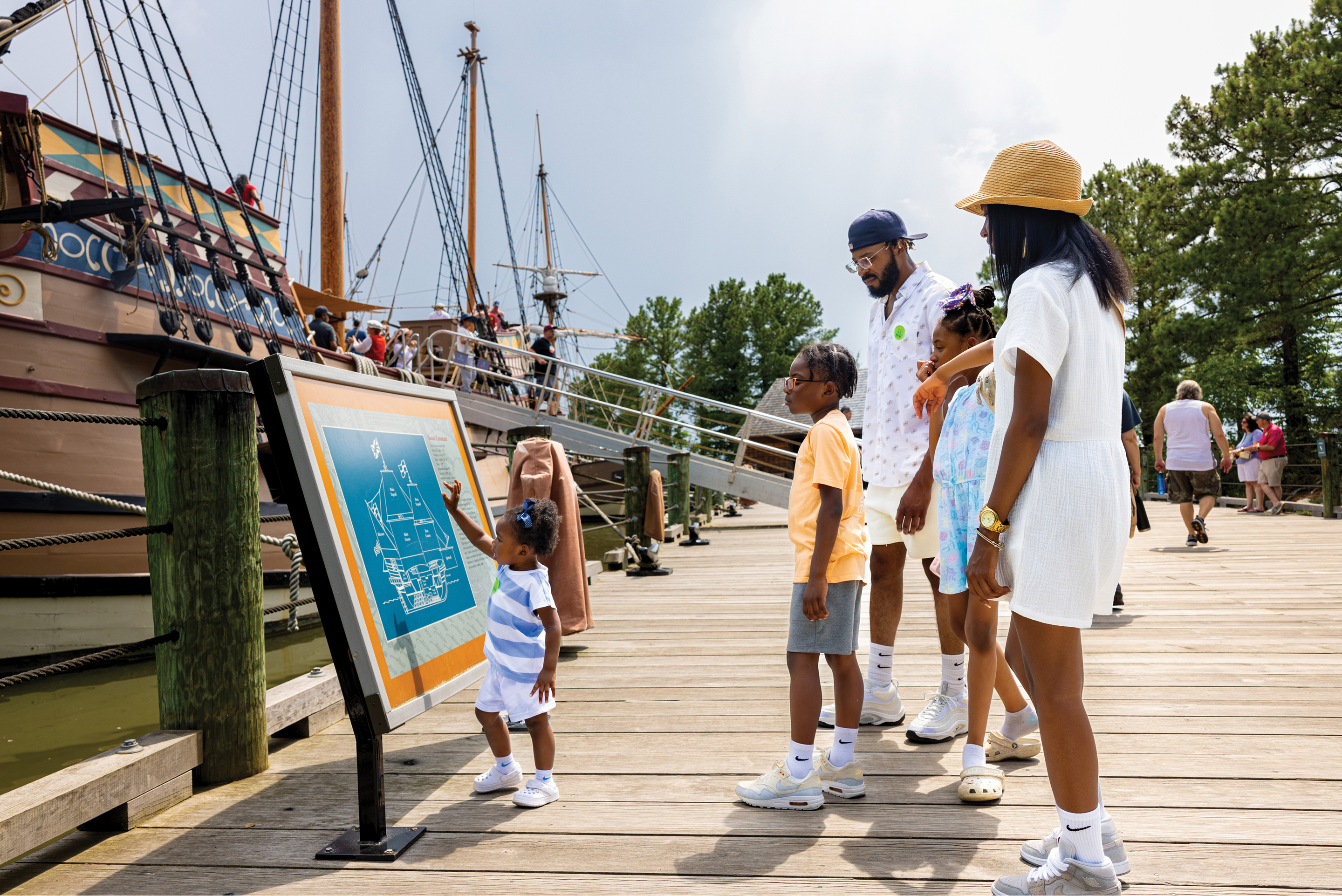 Family on a boardwalk looking at a vintage ship