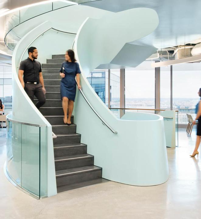 Two people walking down a staircase in a well-lit room with other people around