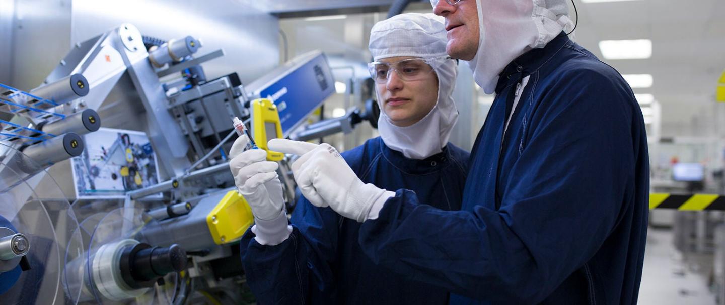 A man and a woman in blue jumpsuits, protective headgear, and gloves reading from a machine