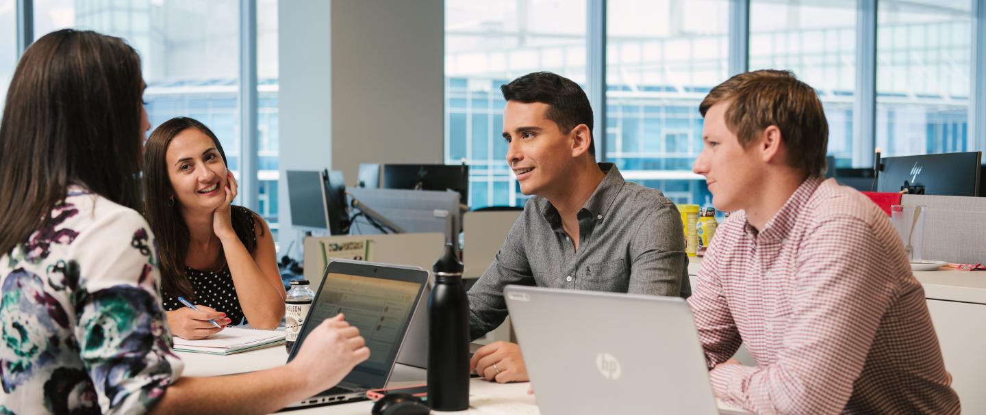 Two women and two men sitting and talking with laptop computers in front of them