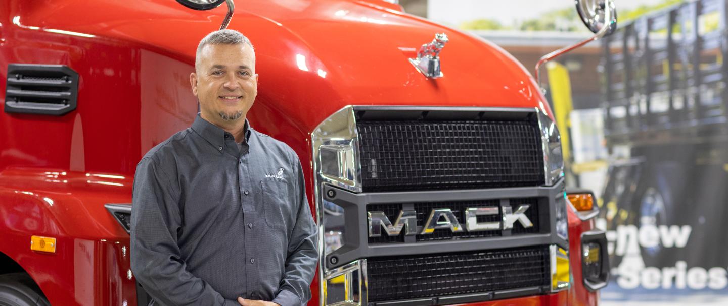 A man standing next to the grille of a large red truck