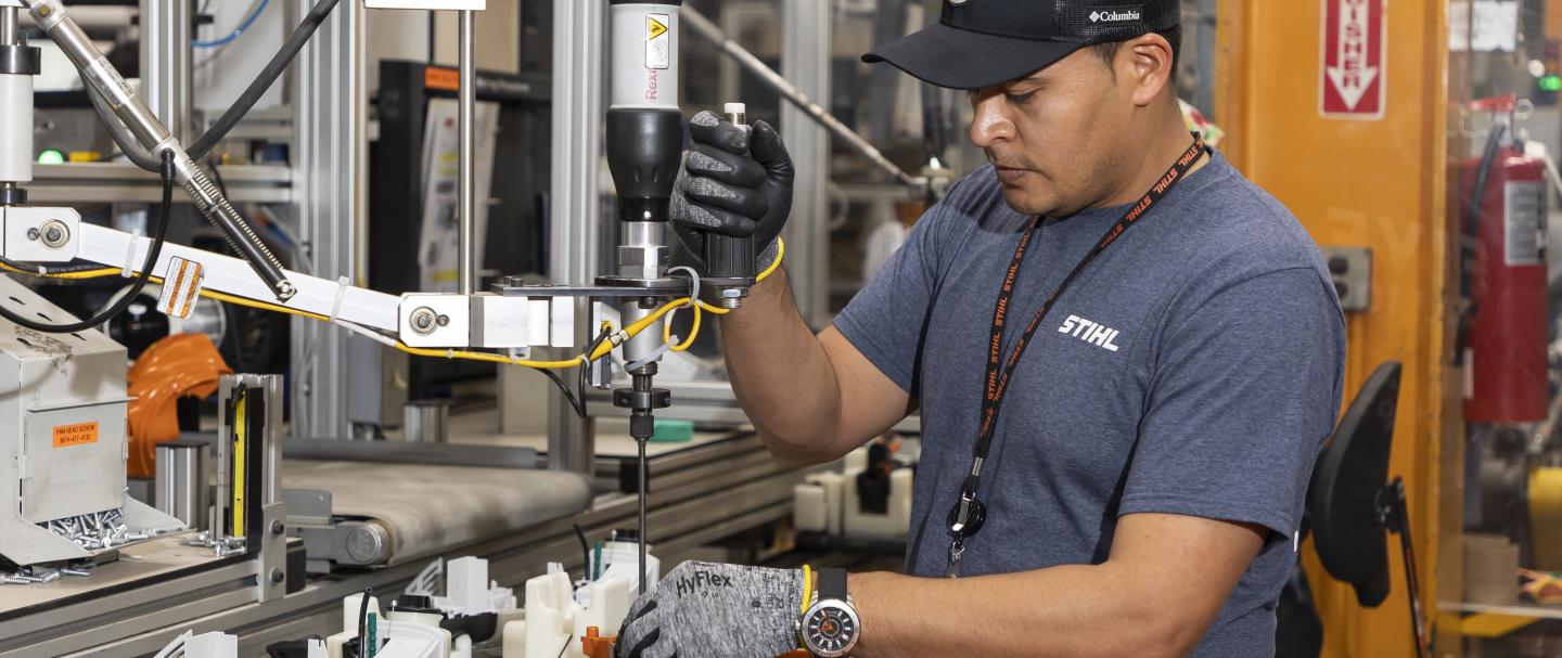 A man wearing a hat operating a machine in a manufacturing facility