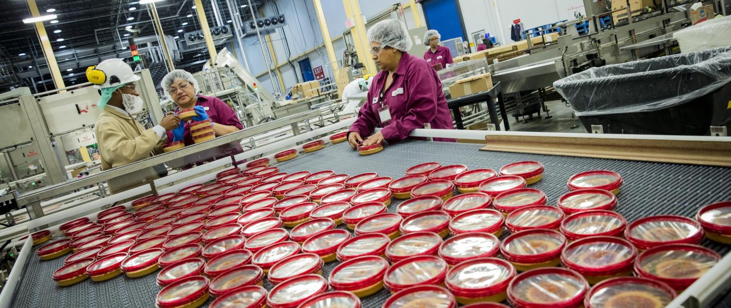 Two women and one man working on a machine organizing tubs of hummus