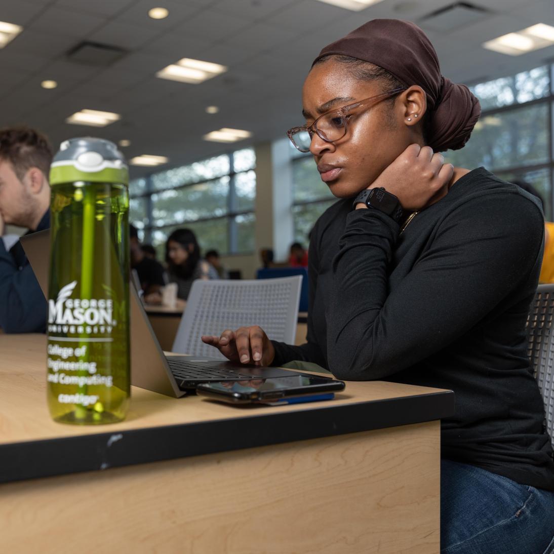 A woman working on a computer with other students in the background