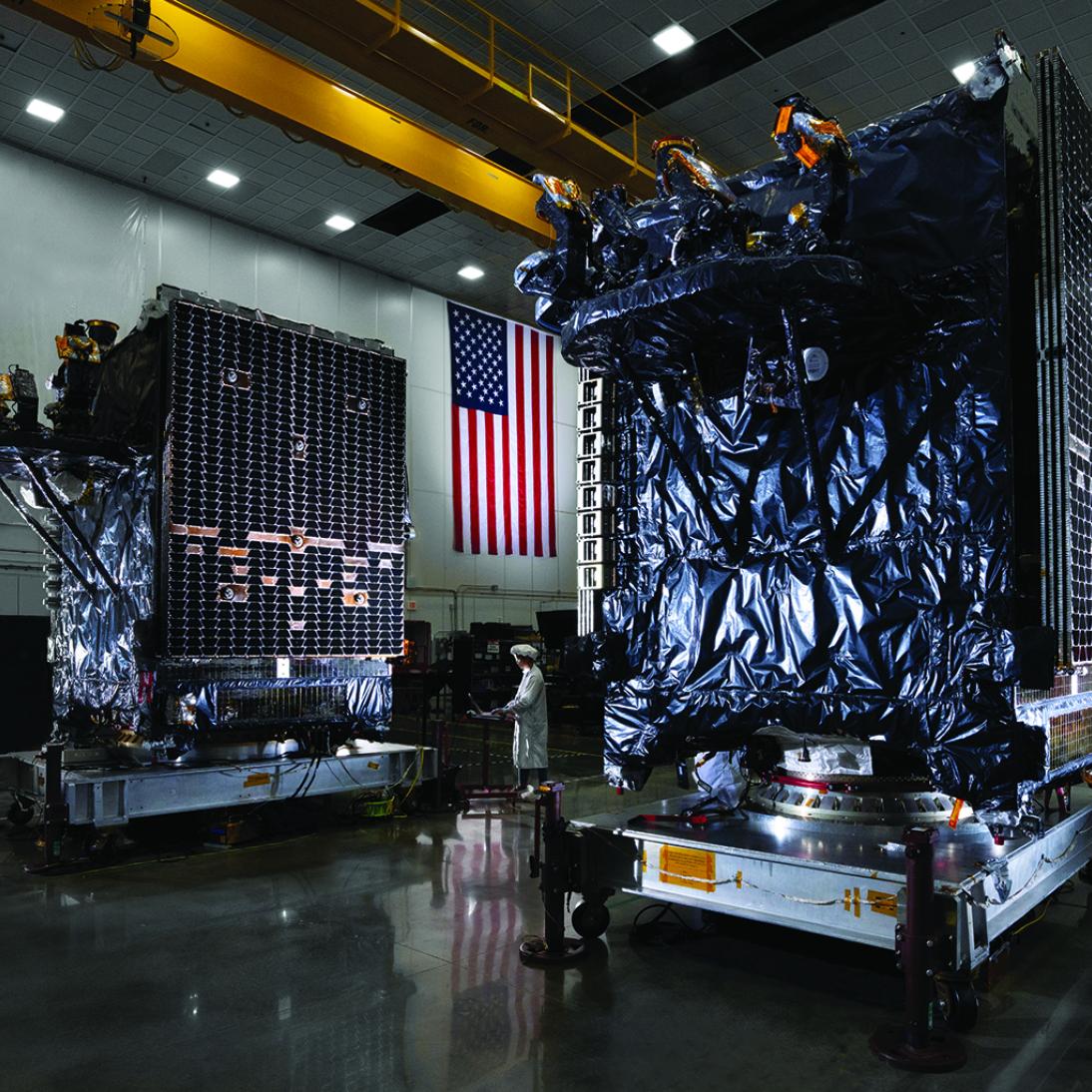 A person working on a computer around two large satellites in a hangar