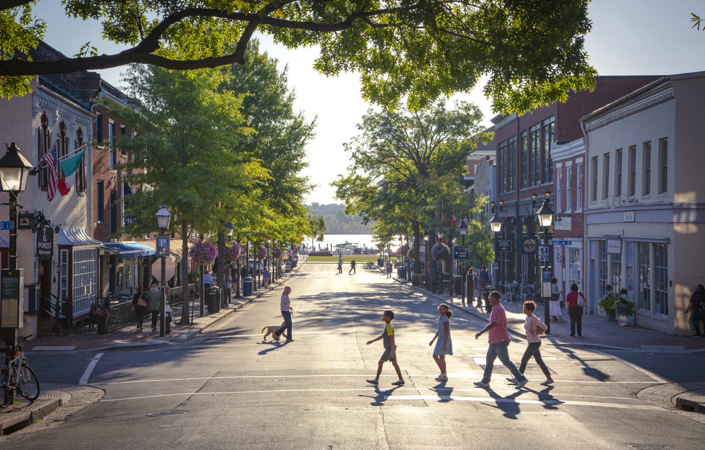 A group of people crossing a street between historic buildings and trees