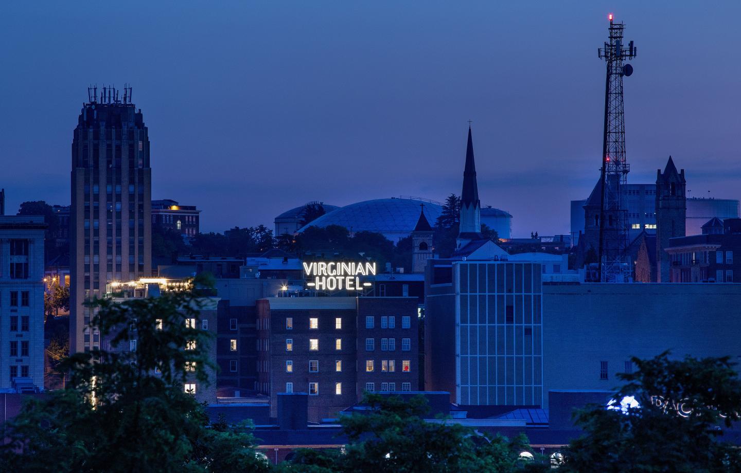 A night skyline with a lit-up sign reading VIRGINIAN HOTEL