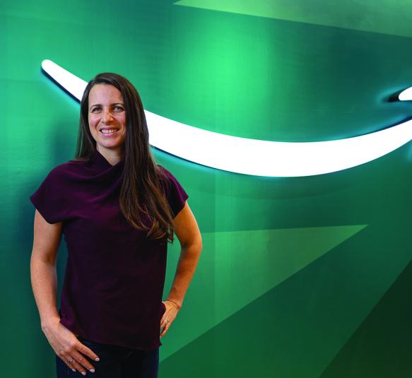 A woman standing in front of a green wall with the Amazon logo