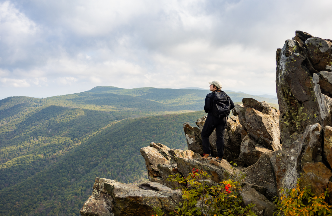 Hikers climbing over large rocks with mountains and clouds in the background
