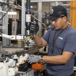 A man wearing a hat operating a machine in a manufacturing facility