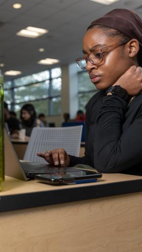 A woman working on a computer with other students in the background