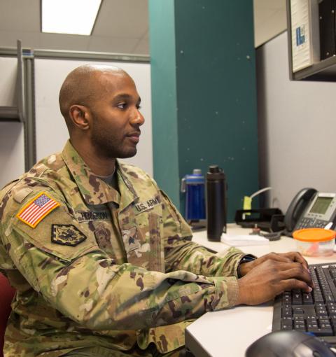 A man in an Army uniform working on a computer